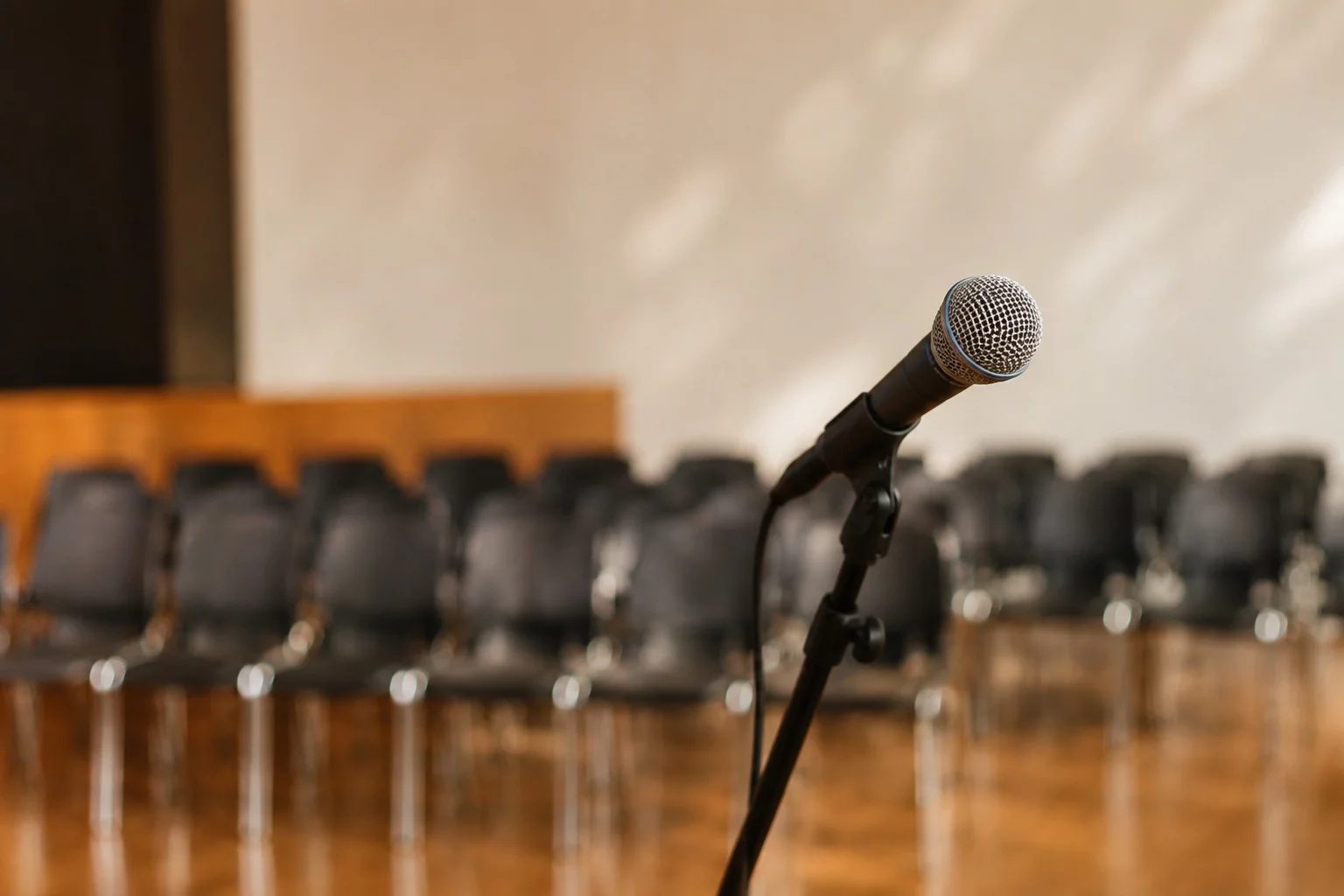 Microfone sobre uma tribuna, com a plateia sentada desfocada ao fundo